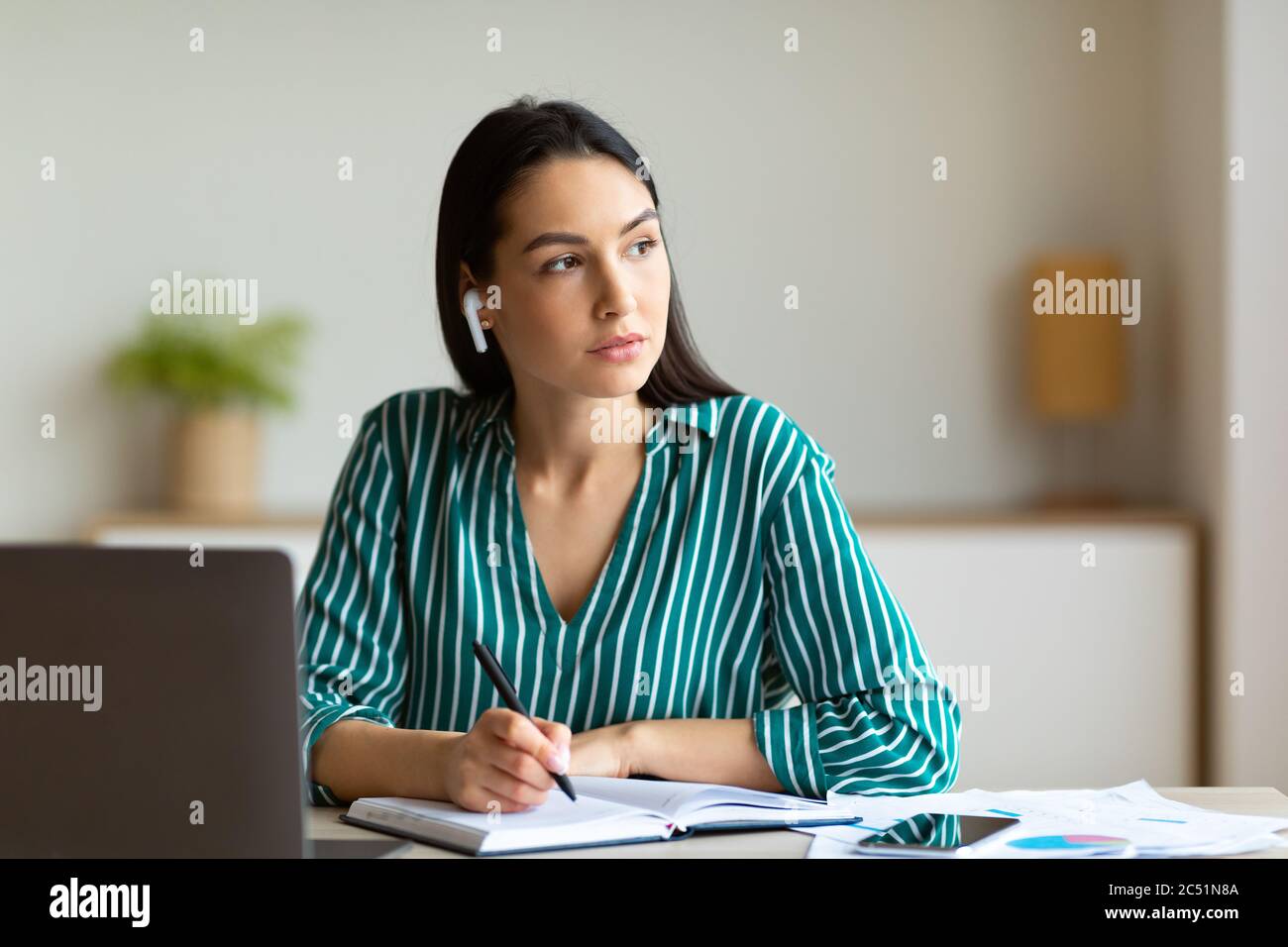 Geschäftsfrau Mit Ohrstöpseln, Die Anrufe Entgegennehmen, Notizen Im Büro Sitzend Stockfoto