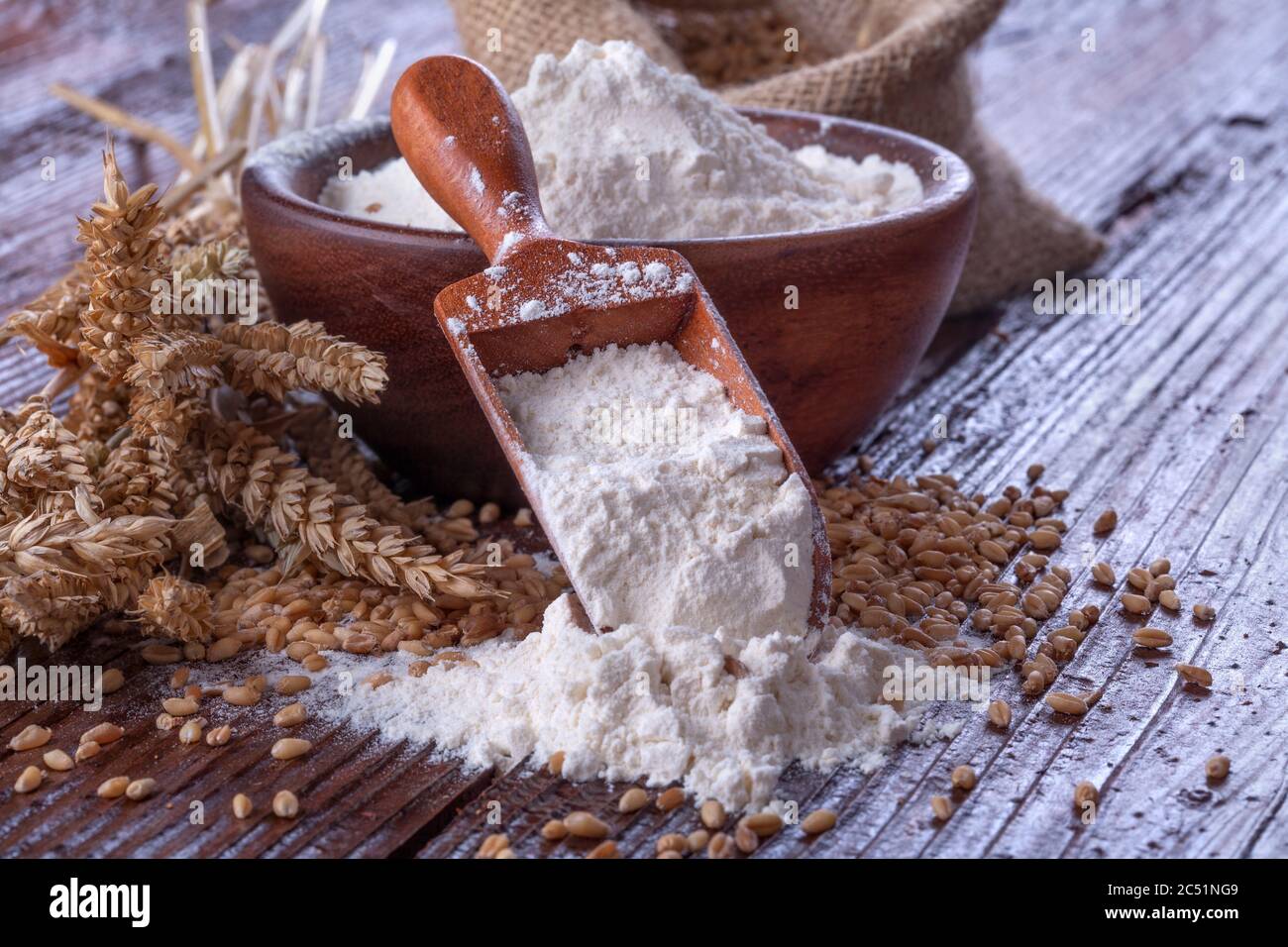 Schaufel Mehl mit Weizen im Hintergrund, auf rustikalen Holztisch. Stockfoto