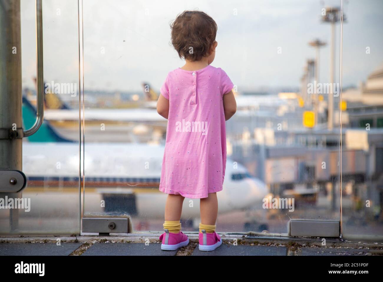 Niedliches Kleinkind Baby in einem rosa Kleid sieht die Flugzeuge am Flughafen an. Warten auf einen Flug. Rückansicht Stockfoto