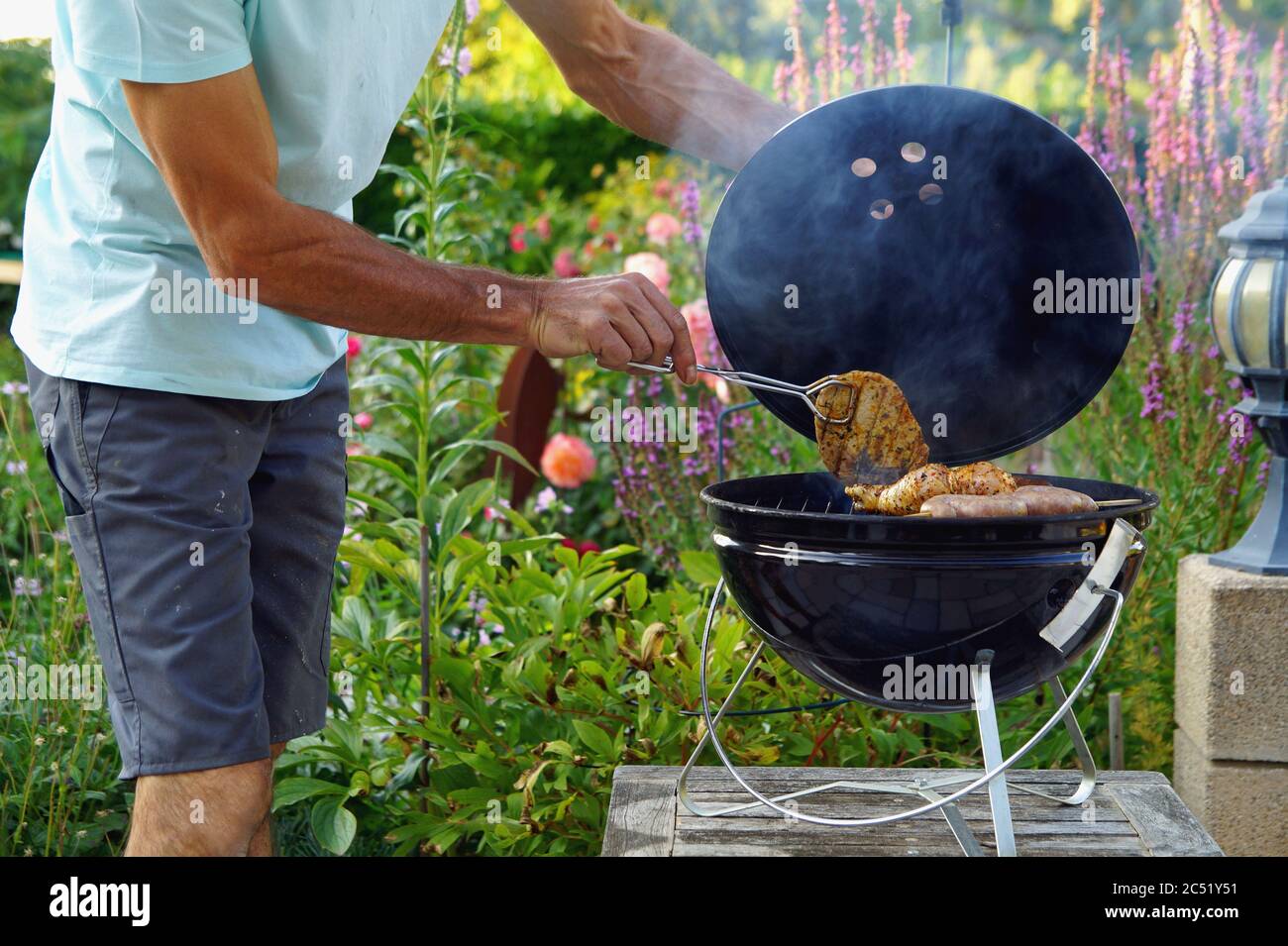 Grill. Die Hand des Mannes grillen mit Zangen, Hand eines Mannes in  Arbeitshosen, der köstliches gegrilltes Fleisch über die Kohlen auf einem  Grill dreht Stockfotografie - Alamy