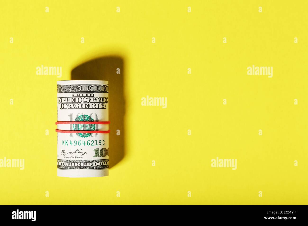 Eine Rolle von hundert-Dollar-amerikanischen Scheinen ist mit einem roten Gummiband auf einem gelben Hintergrund gebunden. Stockfoto