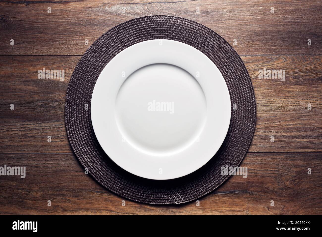 Leere weiße runde Platte mit einer Serviermatte auf Holztisch. Flatlay-Ansicht von oben. Stockfoto