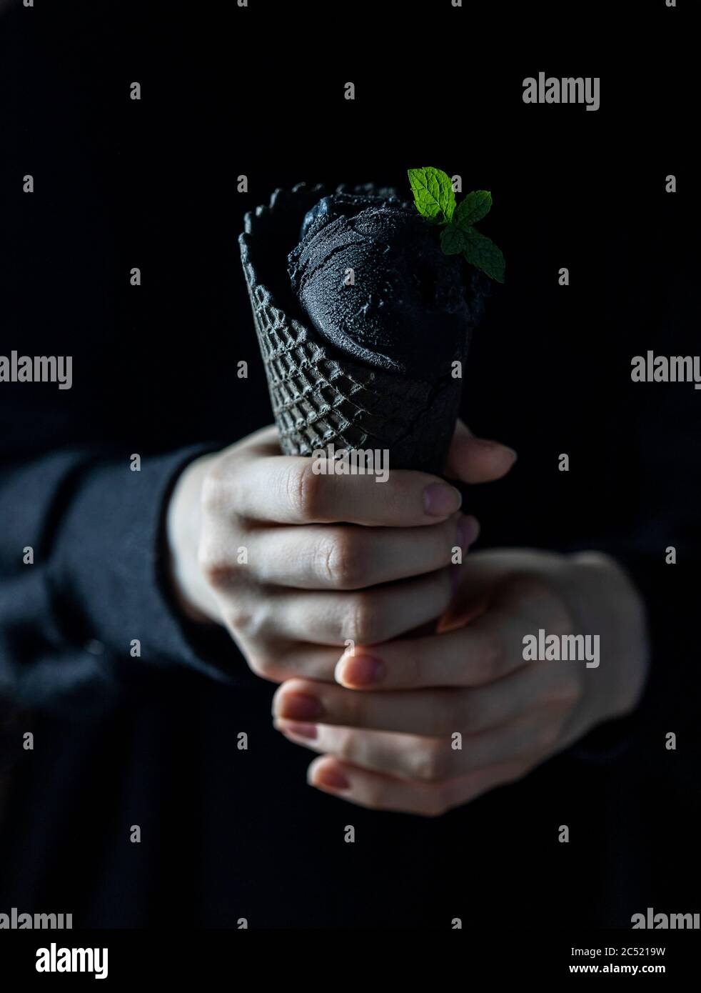 Schwarzes Eis in einem Waffelbecher in weiblichen Händen. Modisches Essen. Speicherplatz kopieren Stockfoto