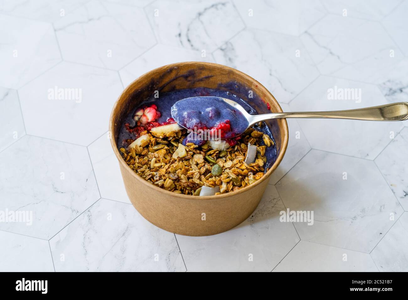 Blaue Matcha Schüssel mit Granola, Heidelbeeren und Banane / gesunde blaue Spirulina Smoothie in brauner Papier Kraftkarton Box. Bio Gesundes Superfood. Stockfoto