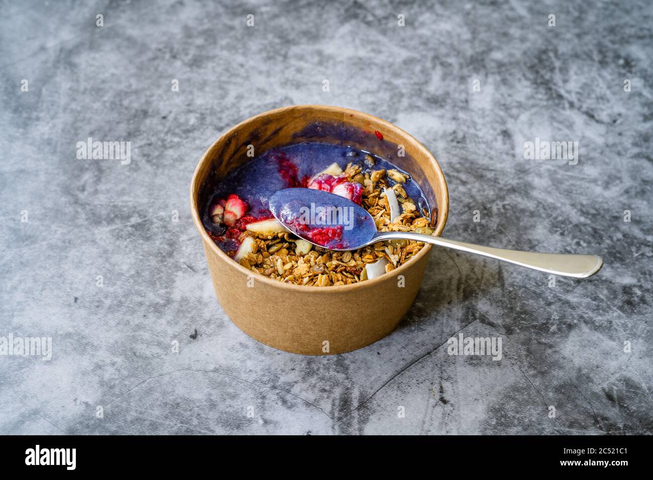 Blaue Matcha Schüssel mit Granola, Heidelbeeren und Banane / gesunde blaue Spirulina Smoothie in brauner Papier Kraftkarton Box. Bio Gesundes Superfood. Stockfoto