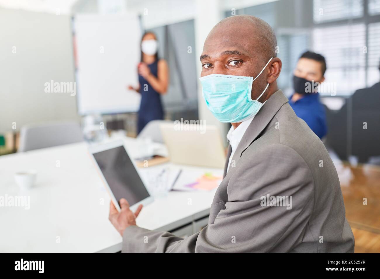 Afrikanischer Geschäftsmann mit Gesichtsmaske über Covid-19 und Tablet-PC in einem Meeting Stockfoto