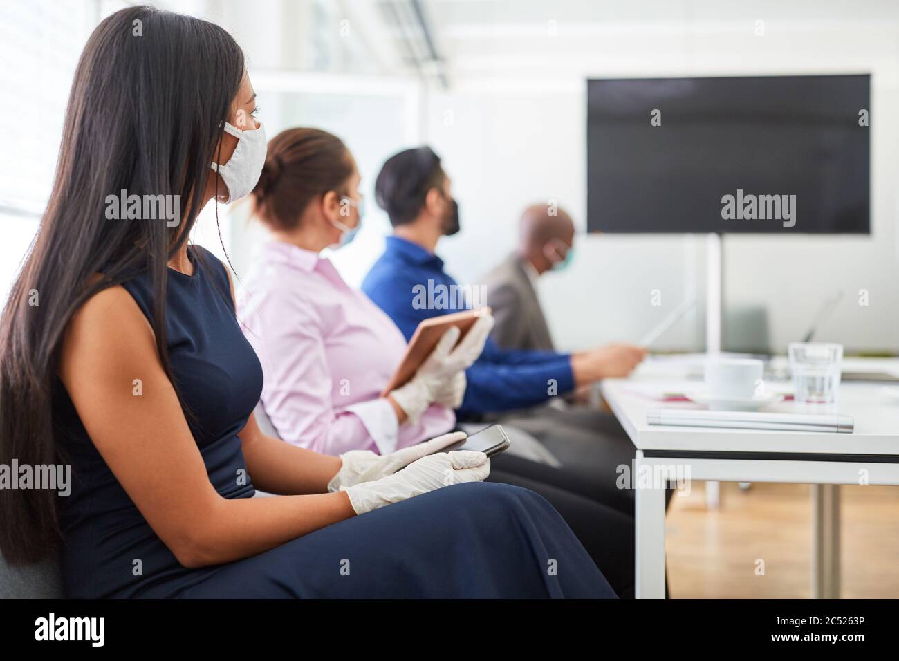 Gruppe von Geschäftsleuten mit Maske wegen Covid-19 in der Sitzung mit Videokonferenz vor einem Monitor Stockfoto