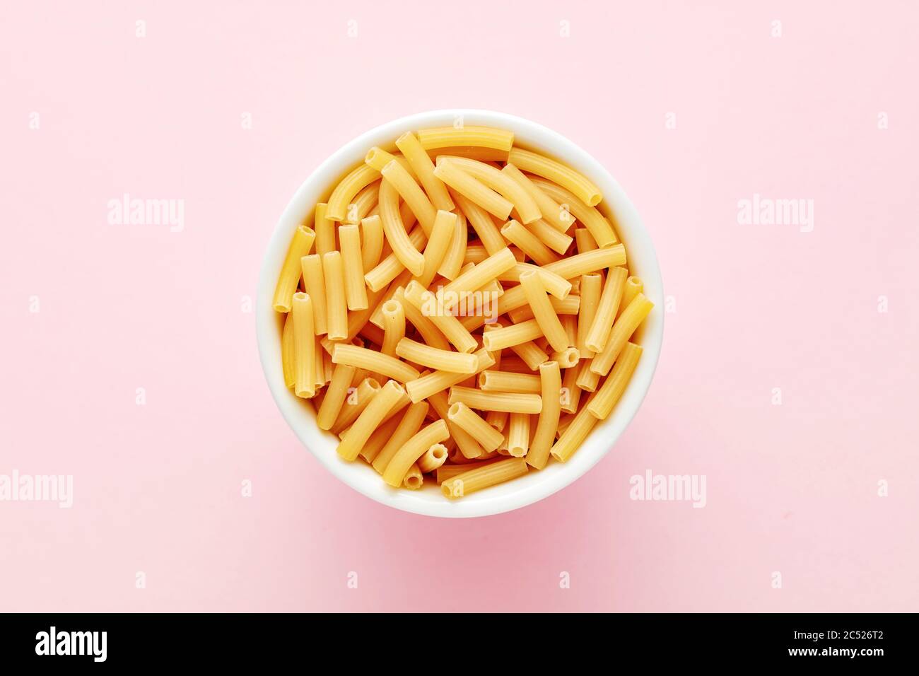 Haufen von Ziti rigati oder Tubini Pasta in einer weißen Schüssel auf rosa Hintergrund. Ansicht von oben. Stockfoto