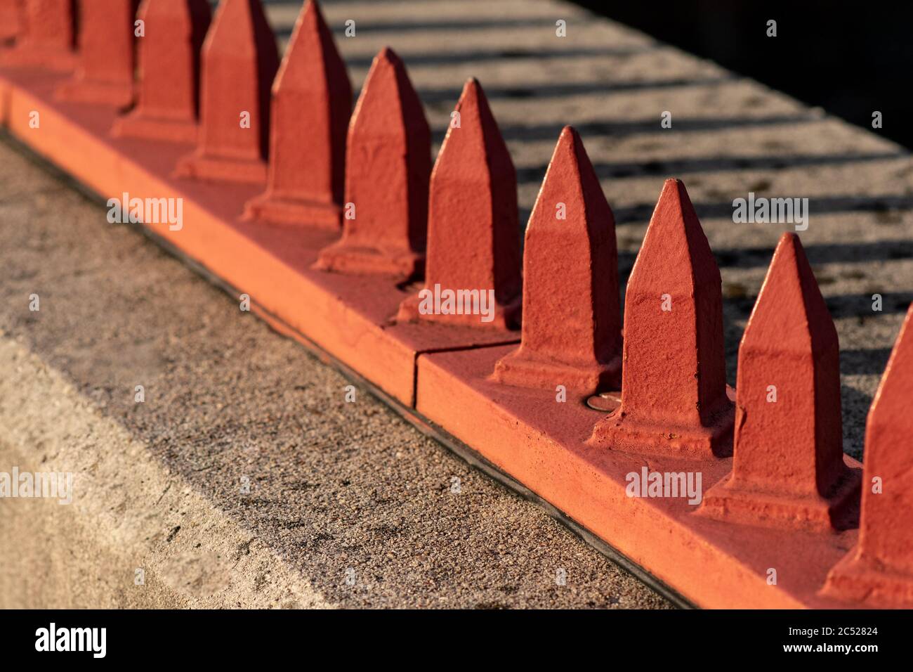 Feindliche Architektur. Rote Metallspitzen auf Zementleiste. Stockfoto