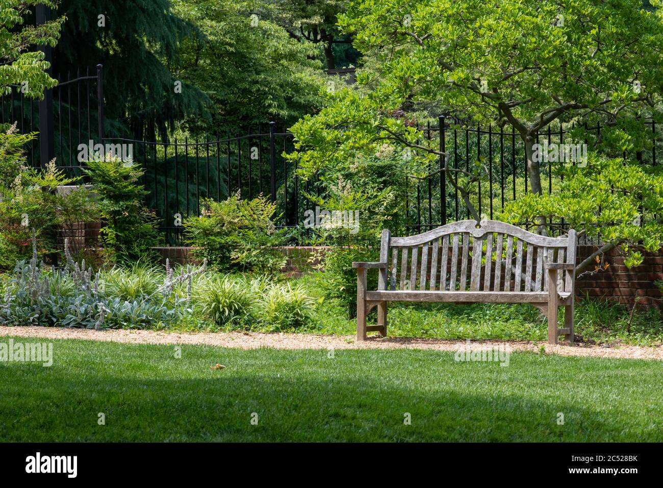 Einsitzige Bank in einem üppigen Sommergarten. Der perfekte Ort, um ein Buch im Freien zu lesen. Stockfoto