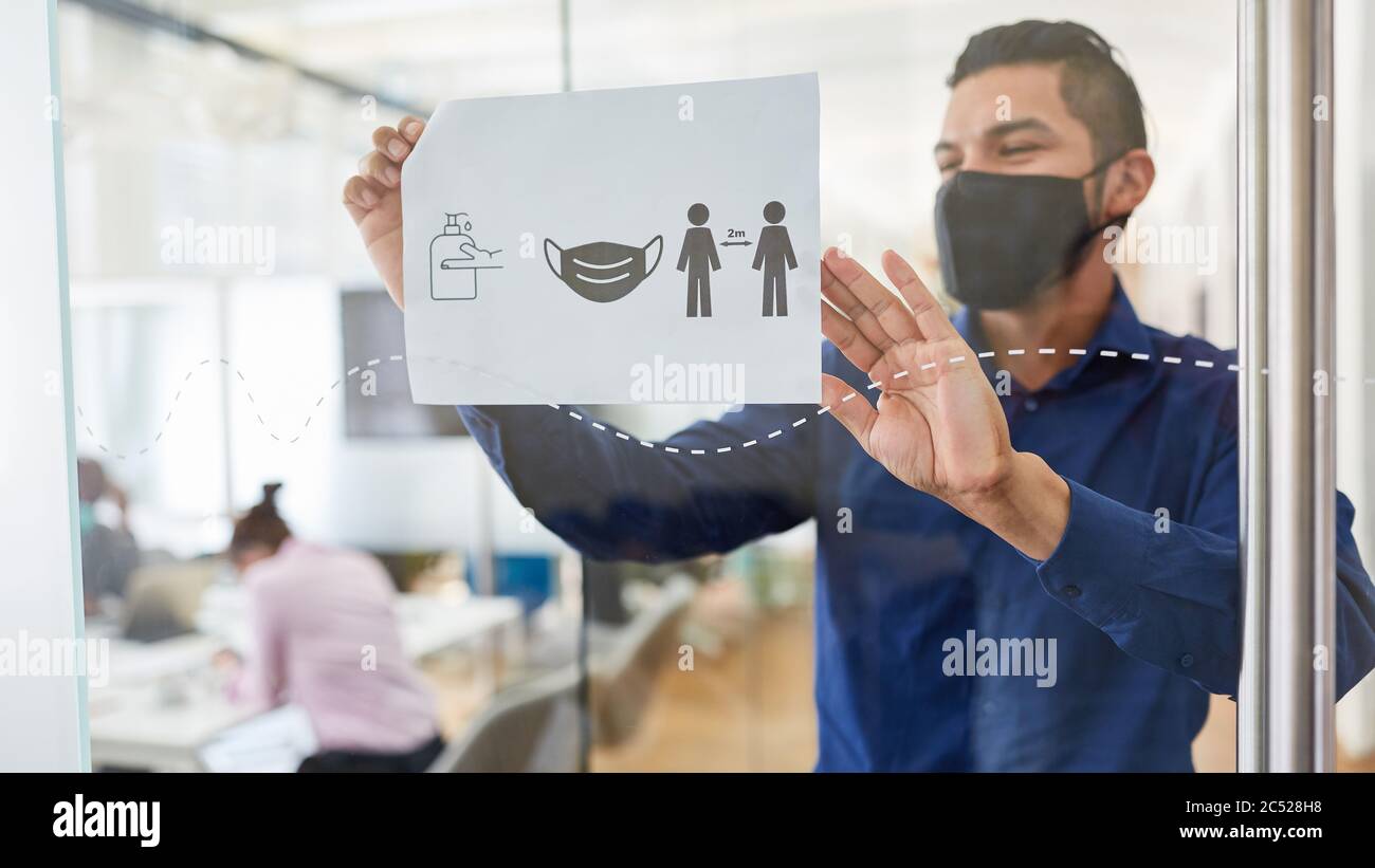 Geschäftsmann mit Gesichtsmaske wegen Covid-19 befestigt Tafel mit Hygienevorschriften im Büro Stockfoto