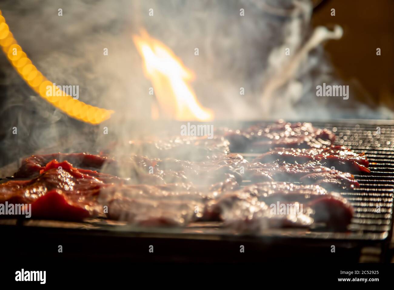 Abends werden auf einem Grill leckere saftige Steaks am offenen Feuer gegrillt. Nahaufnahme, Weichfokus. Rauch wird hervorgehoben Stockfoto