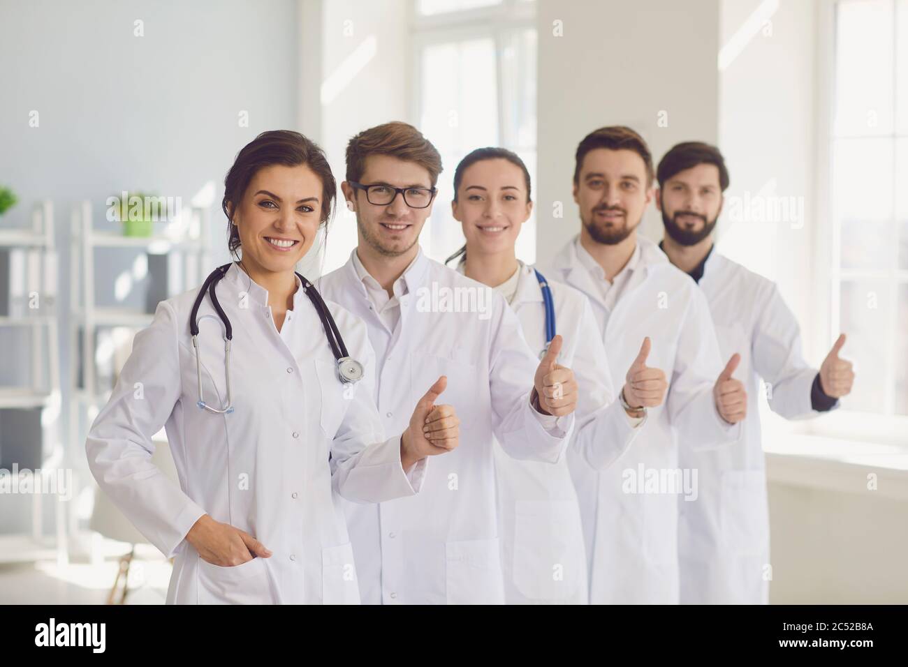Junge lächelnde Ärzte Team Portrait mit Daumen nach oben Geste in modernen klinischen Krankenhaus Büro. Stockfoto