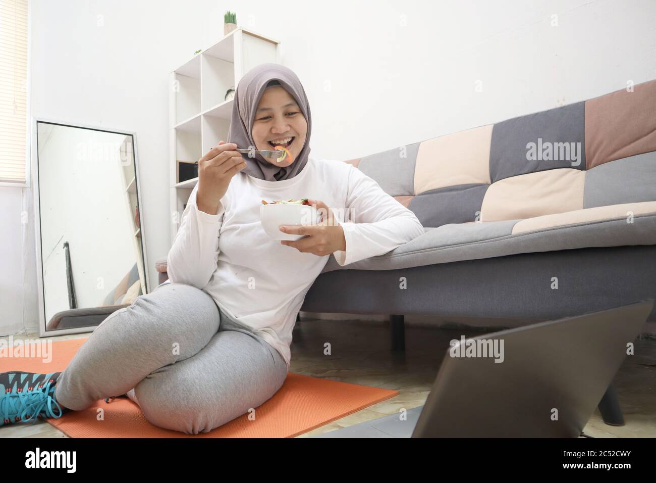 Asiatische muslimische Frau trägt Hijab gesunde Lebensmittel, grüne Gemüse Salat essen, nach dem Training zu Hause, halten Sie sich gesund und fit während der neuen normalen Lebensstil Co Stockfoto