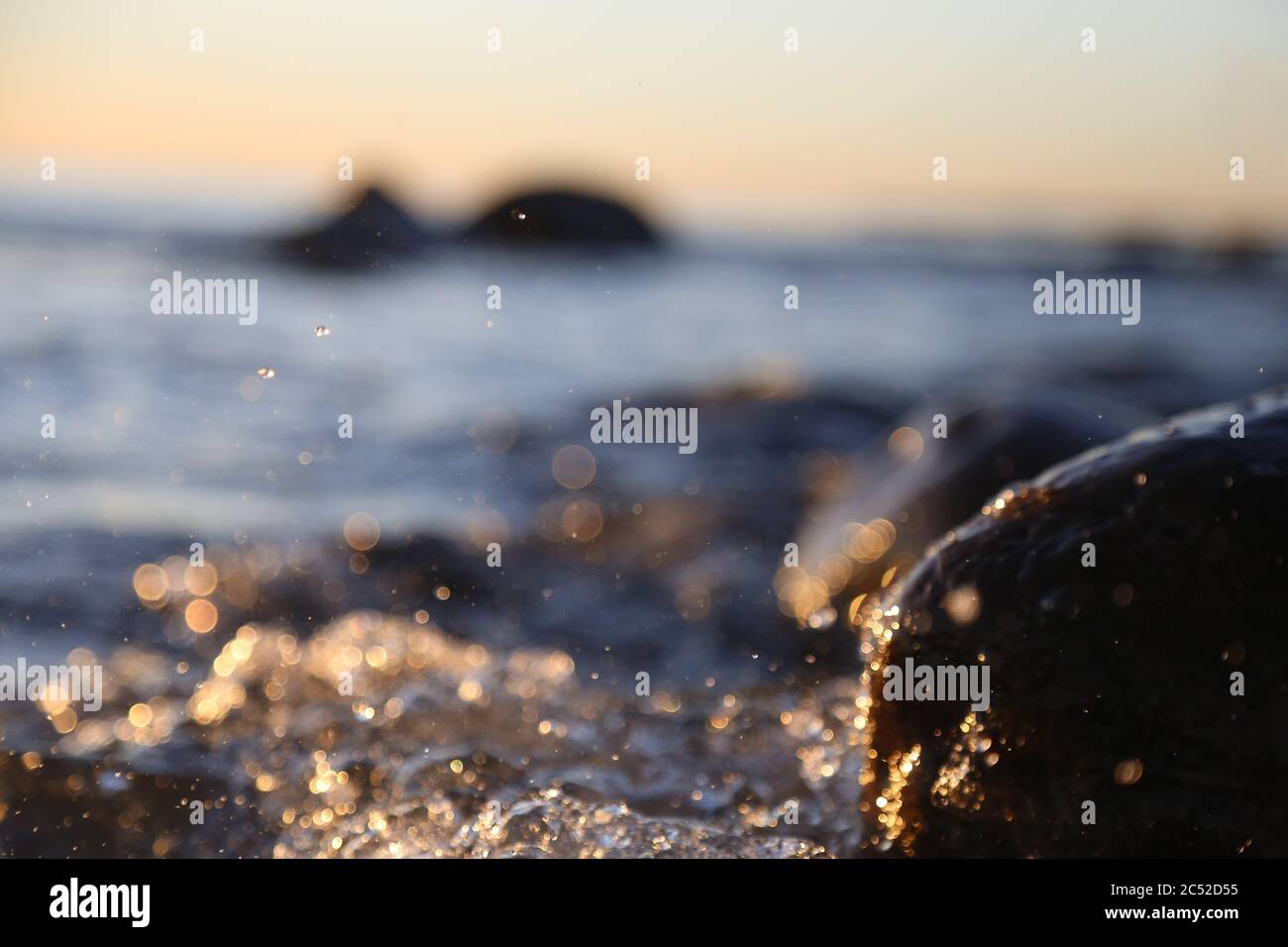 Nahaufnahme von Meereswellen, die auf einer nassen Küste brechen Steine Sommer Sonnenuntergang, Wasserspritzer, Sonnenstrahlen, Reflexionen auf Wassertropfen. Stockfoto