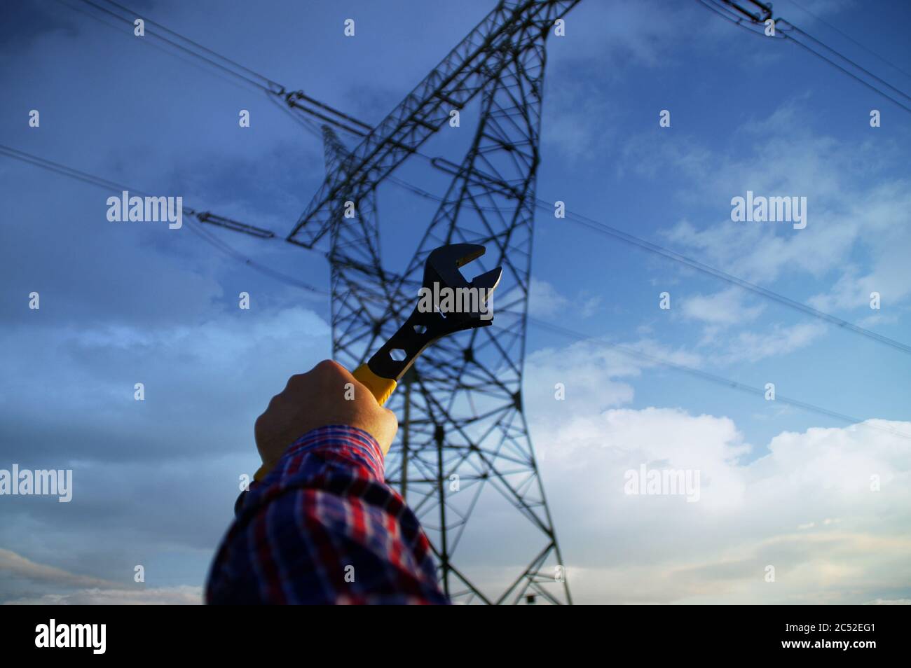 Industrie- und Stromleitungswartungskonzept. Schraubenschlüssel in der Hand mit Silhouette von elektrischen Pylon im Hintergrund. Energienetzdienst. Stockfoto