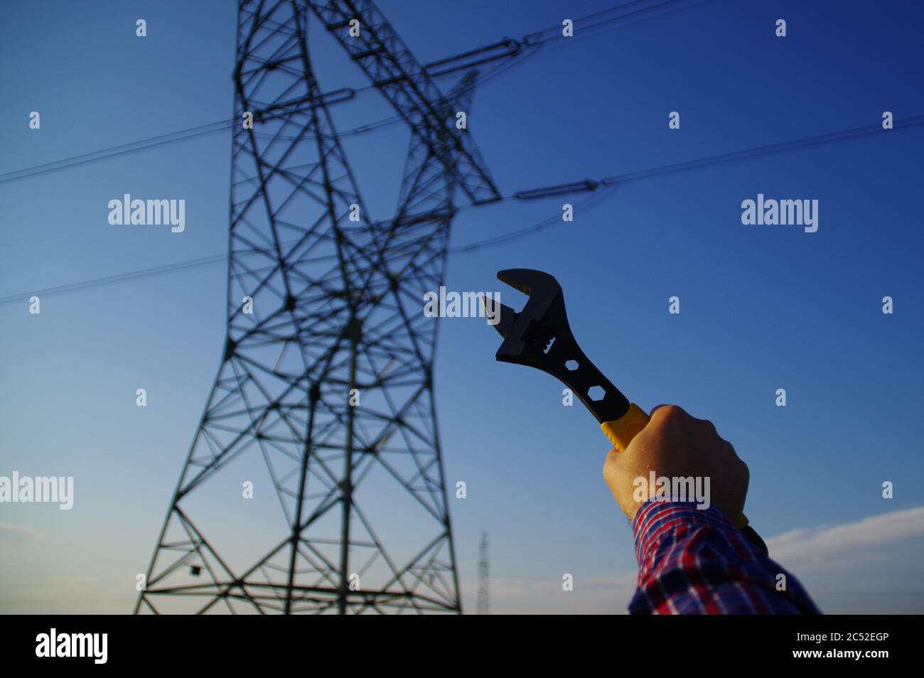 Industrie- und Stromleitungswartungskonzept. Schraubenschlüssel in der Hand mit Silhouette von elektrischen Pylon im Hintergrund. Energienetzdienst. Stockfoto
