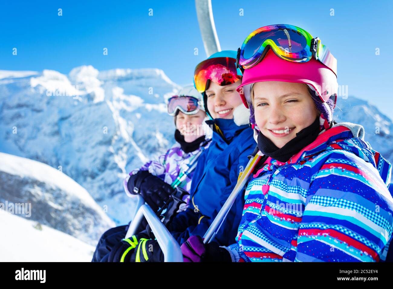 Glücklich lächelndes Mädchen sitzen auf Sessellift trägt Helm und helle Ski-Outfit mit Freunden über schönen Berggipfel Stockfoto