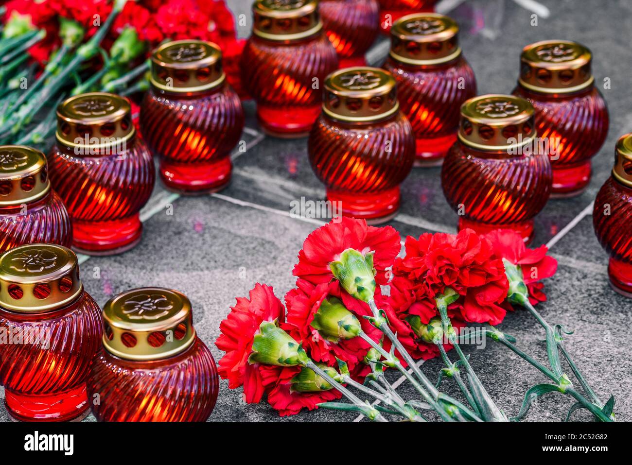 Rote Nelken auf einer Marmorplatte und Begräbnislampen. Symbol der Trauer, Blumenauflegung an der Gedenkstätte. Stockfoto