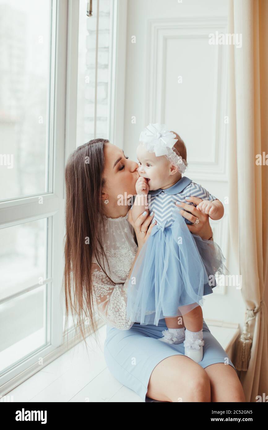 Lächelnde Mutter sitzt auf einer Fensterbank und küsst ihre kleine Tochter Stockfoto