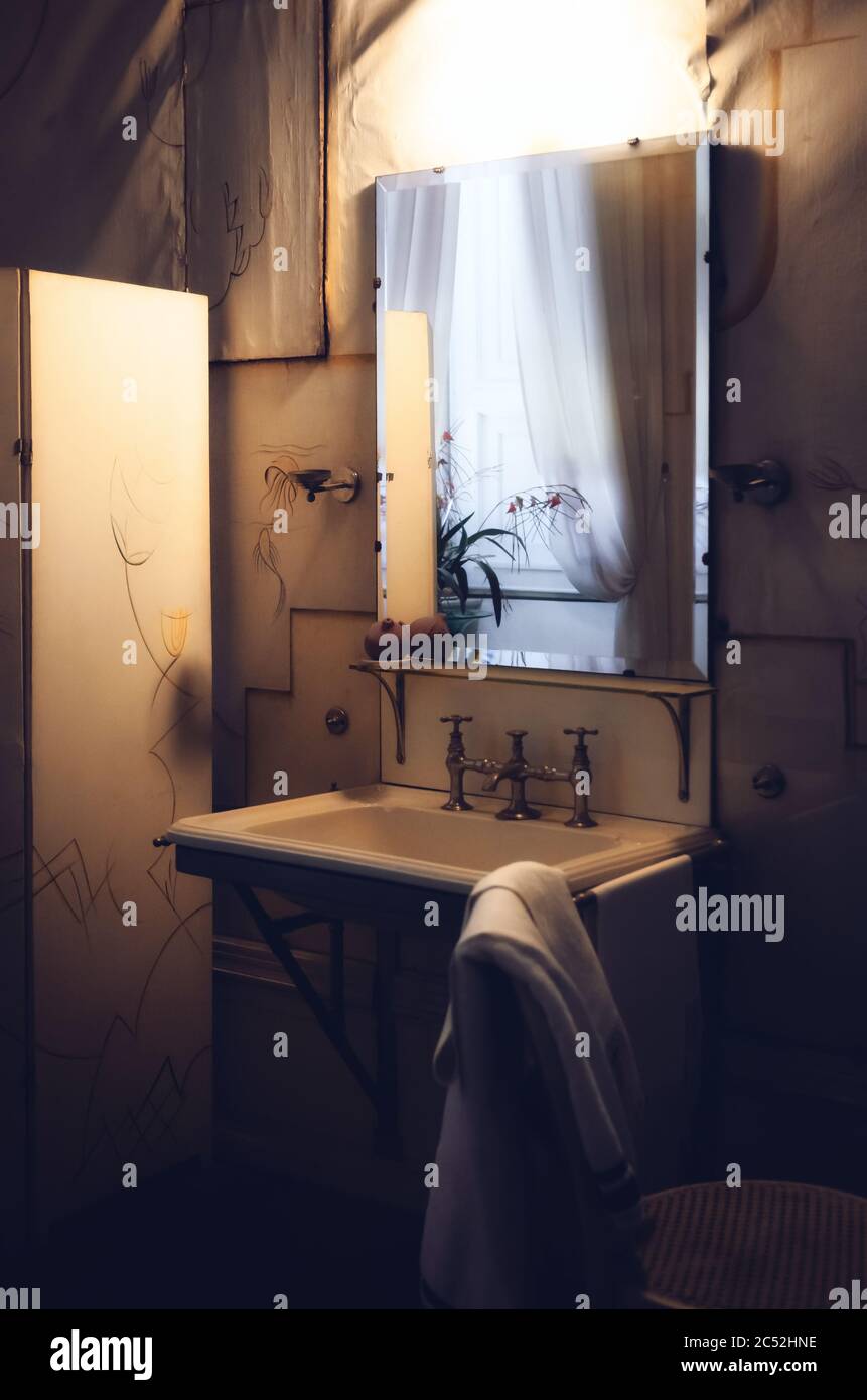 Sehr altes und reiches Badezimmer aus dem Anfang des XX Jahrhunderts, mit Spiegel, Wasserhahn und Waschbecken, in dunklem Umgebungslicht Stockfoto