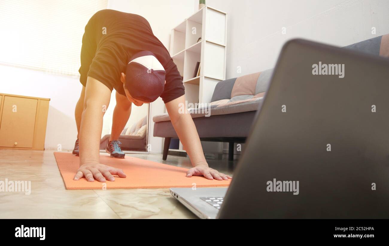 Asiatische männliche tun Übung zu Hause, während Online-Video-Anleitung auf Laptop, Indoor-Home-Workout-Konzept, gesund zu halten auf neue normale Lebensweise Stockfoto