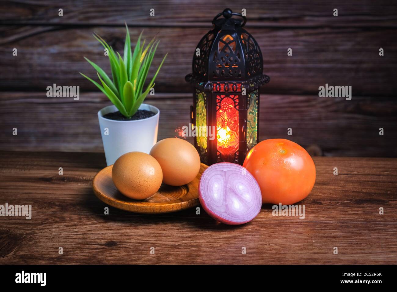 Eier, Tomaten und Zwiebeln auf einem Tisch neben einer Laterne und Topfpflanze Stockfoto