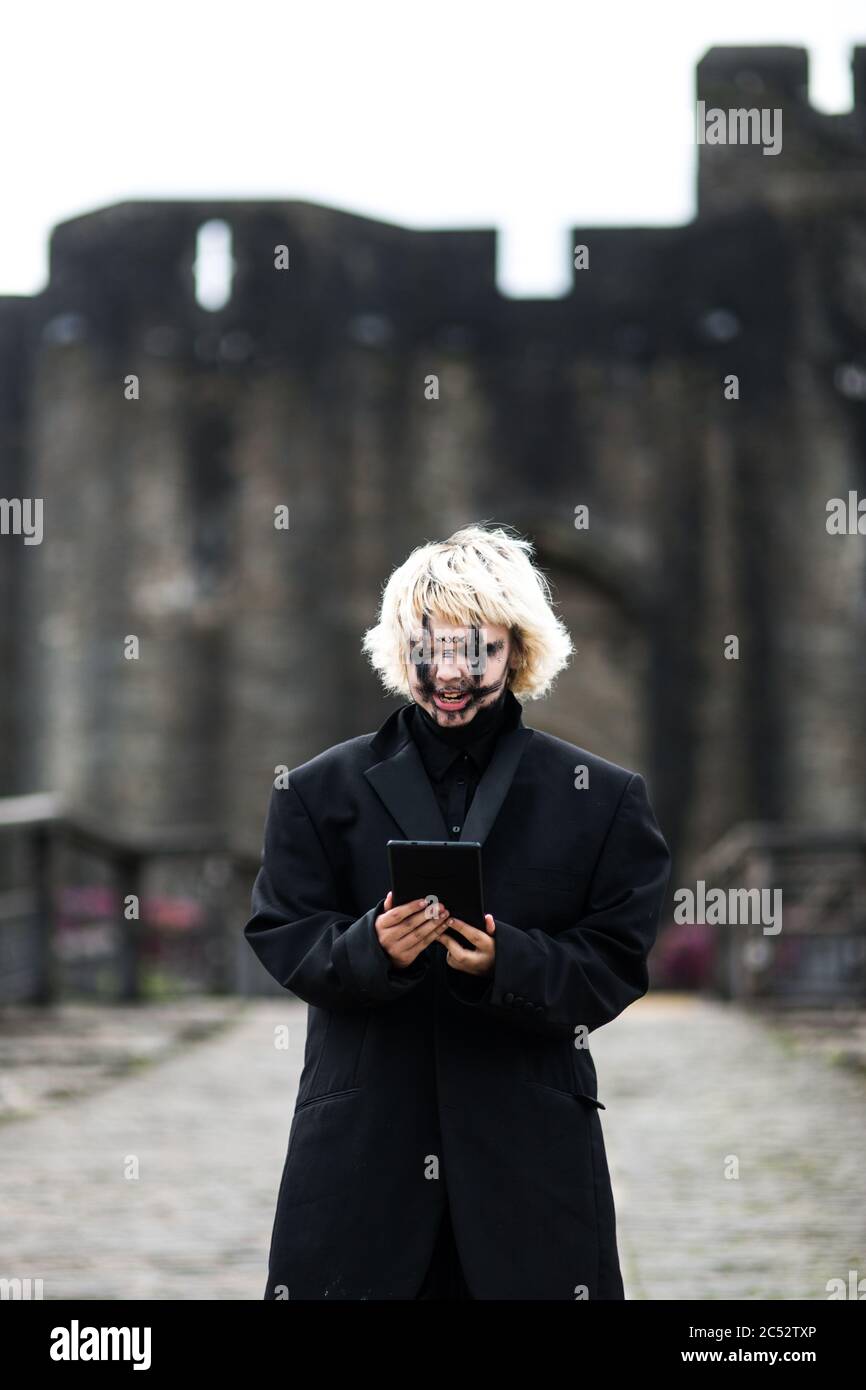 Ein edgy Millennial Mädchen in schwarz mit schwarzem Make-up steht vor dem Schloss und liest etwas auf ihrem Handy Stockfoto