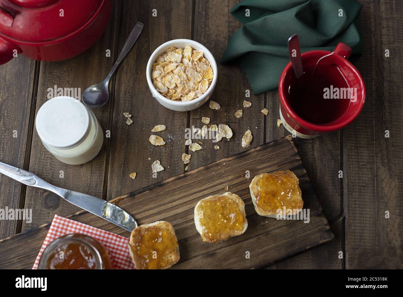 Frühstückstisch mit einer Schüssel Müsli, einer Tasse Tee und einigen Brötchen mit Marmelade Stockfoto