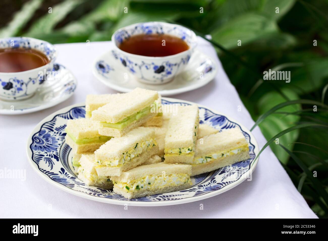 Nachmittagstee im Garten, Fingersandwiches mit Gurken und Eiersalat und Tee auf hellem Hintergrund. Stockfoto