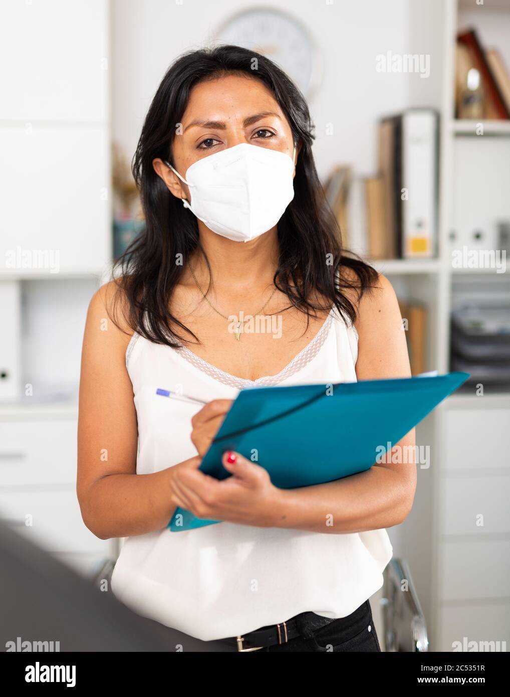 Fokussierte Geschäftsfrau in Einweg-Gesichtsmaske Aufschreiben Aufgaben im Büro. Die Vorgiftungen der Virusinfektion verbreiten sich Stockfoto