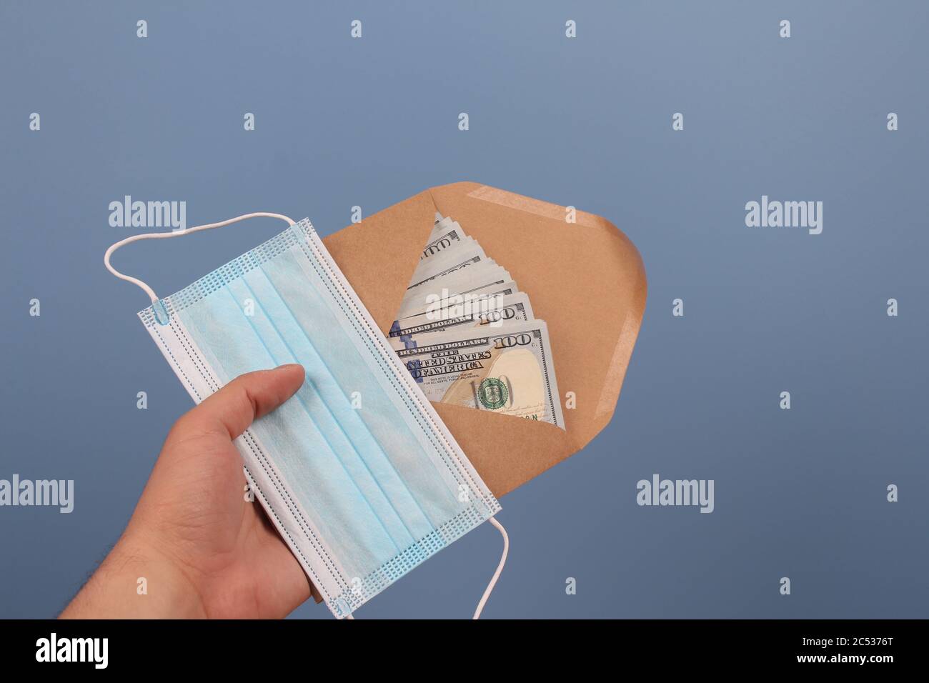 Mann hält Einweg-Gesichtsmaske und Umschlag mit Papier Geld Banknoten auf blauem Hintergrund mit Copyspace. Geldwäsche und Bestechung Konzept in Stockfoto
