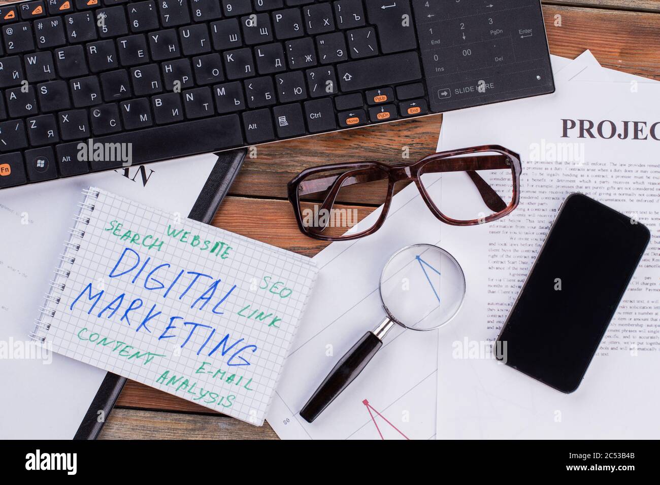 Digitales Marketing auf Notizblock und diverse Business Papers auf braunem Hintergrund. Stockfoto