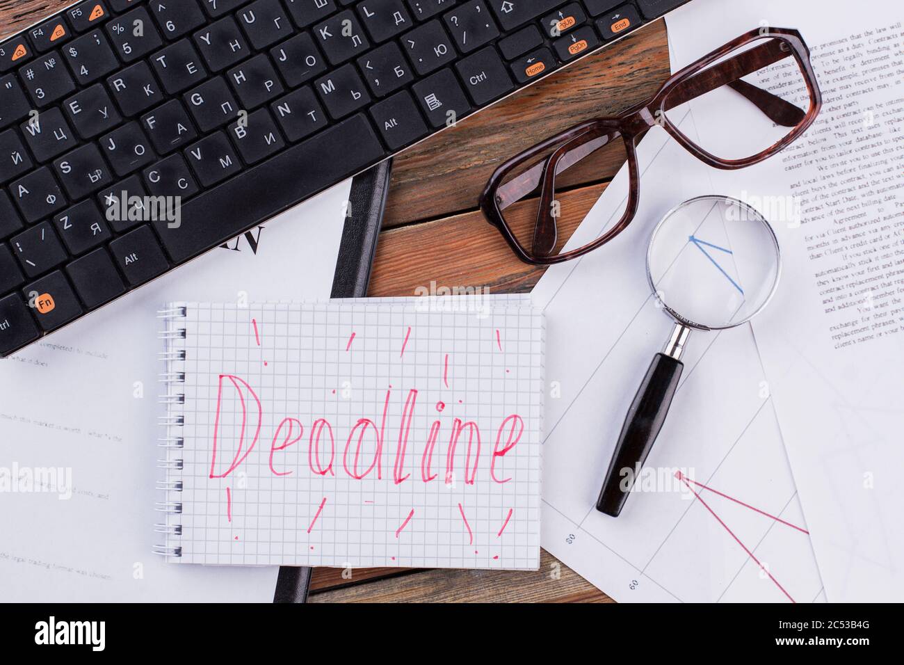 Notizblock mit Lupe, Brille und Tastatur auf Holzhintergrund. Stockfoto