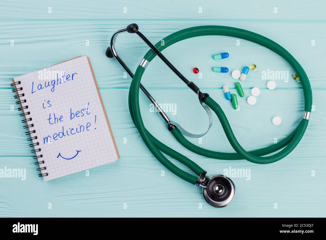 Notizblock mit medizinischem Stethoskop und in der Nähe von Medikamentententabletten auf blauem Hintergrund. Stockfoto