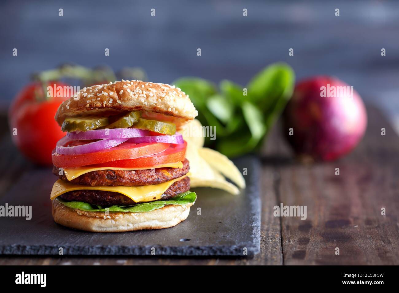 Vegetarischer Cheeseburger mit zwei Fleischersatzpasteten, Scheiben geschmolzenem Käse, Zwiebeln, Gurken, Salat und Tomaten auf einem frischen Sesamsamen BU Stockfoto