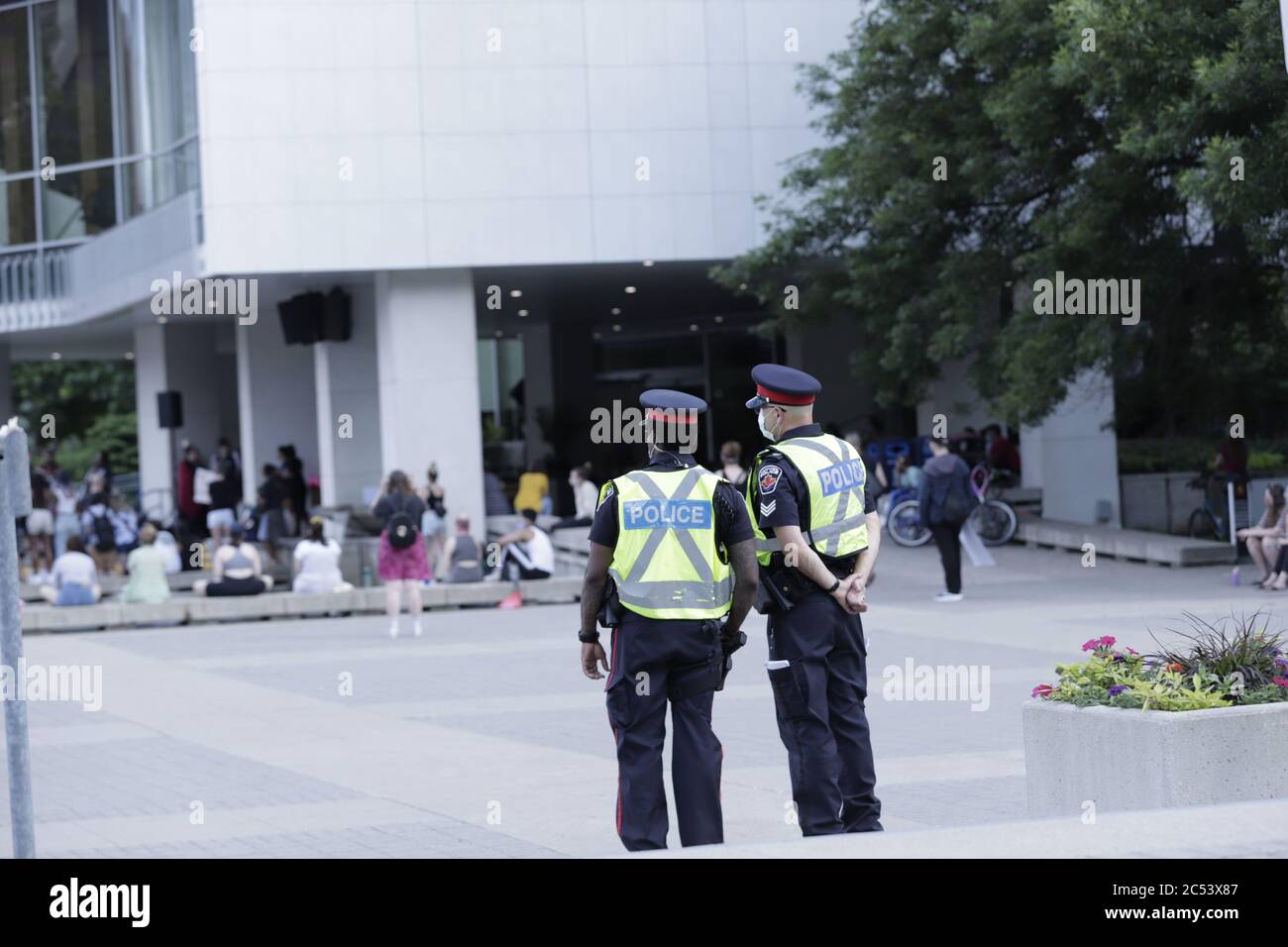 Zwei Polizisten beobachten aus der Ferne, während sich Menschen zu friedlichen Anti-Rassismus-Protestaktionen gegen BLM in Hamilton City Hall, Ontario, Kanada, versammeln Stockfoto