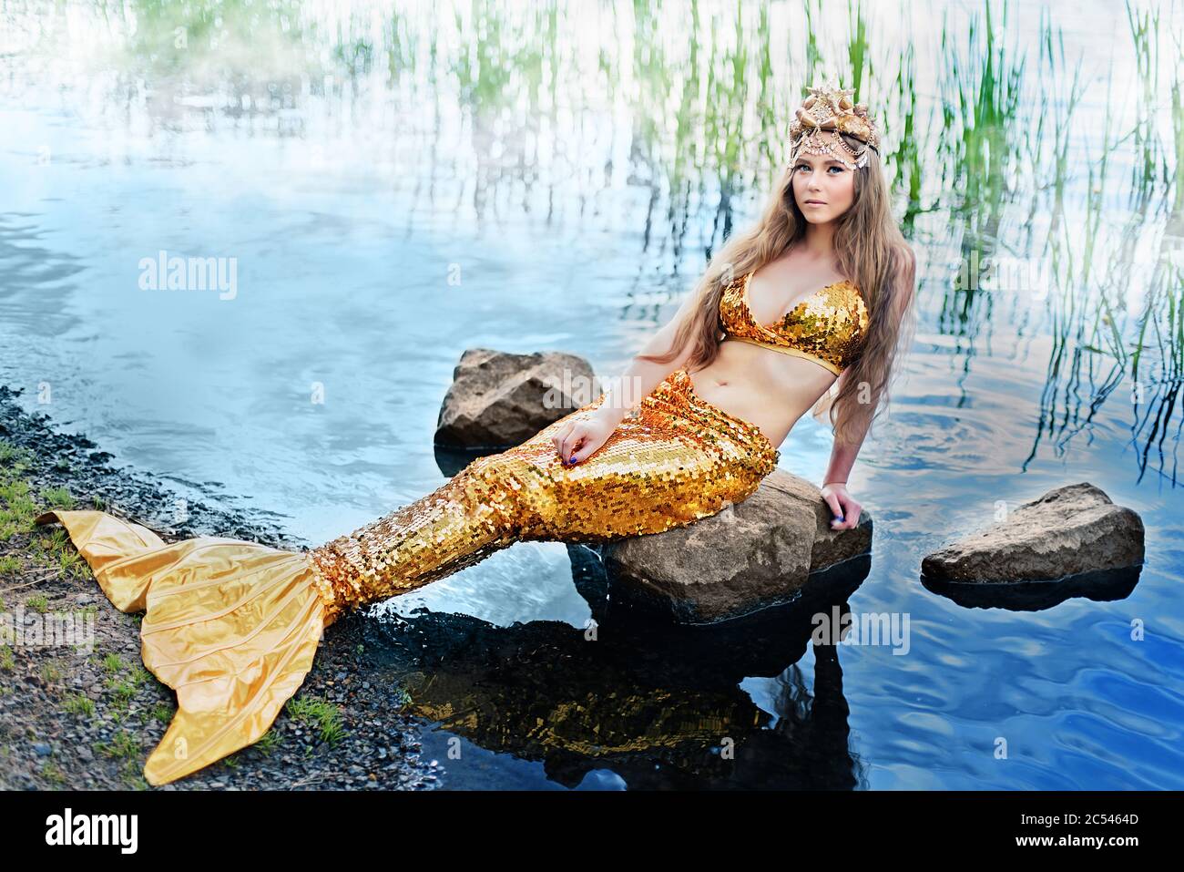 Fantasy Frau echte Meerjungfrau Mythos Göttin des Meeres mit goldenen  Schwanz sitzt in Sonnenuntergang auf Felsen.. Gold Haar Krone Muscheln  Perlen Schmuck. Meerjungfrau sitzt darauf Stockfotografie - Alamy