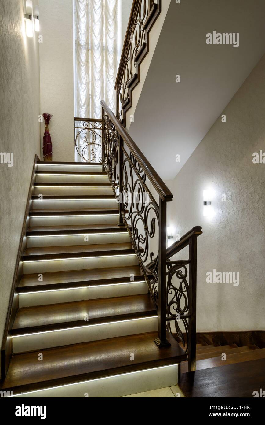 Inneneinrichtung eines Wohnhauses oder Hotels. Schöne Treppe mit LED-Leuchten. Wohndesign im modernen Stil. Moderne Holztreppe mit geschmiedetem r Stockfoto