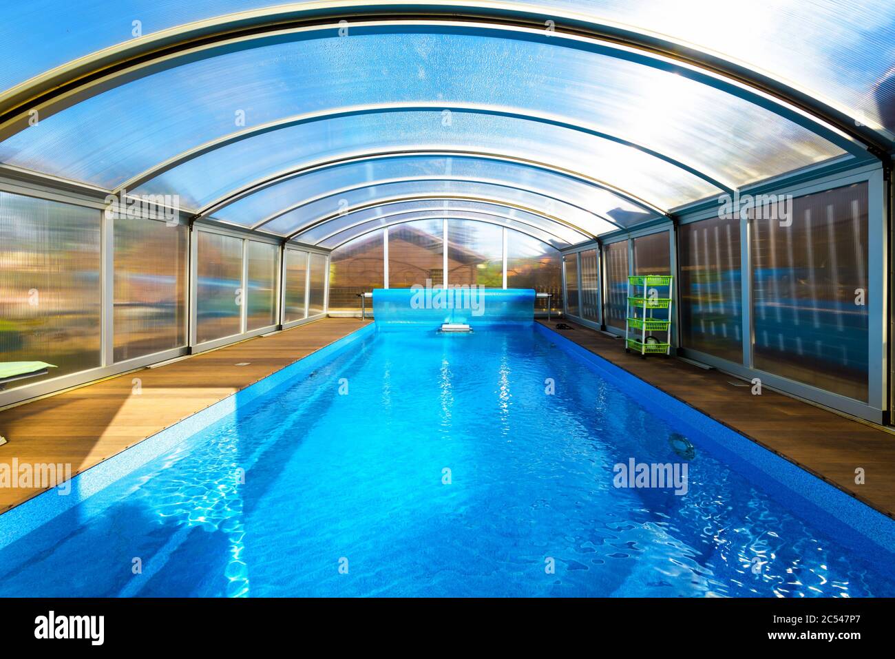 Schwimmbad mit blauem Wasser und transparentem Kunststoffzelt. Modernes Pooldesign mit zusammenklappbarer Wand und Dach. Schöner moderner Pool im Hinterhof des Hauses Stockfoto