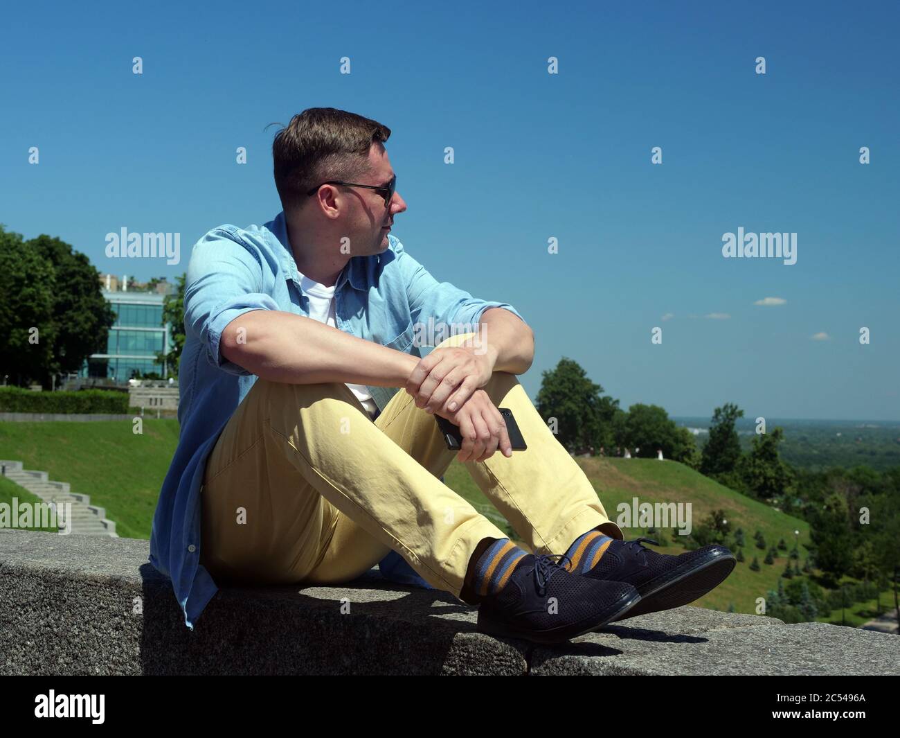 Entspannung im Sommer. Der Typ schaut in die Stadt, während er im Park sitzt. Stockfoto
