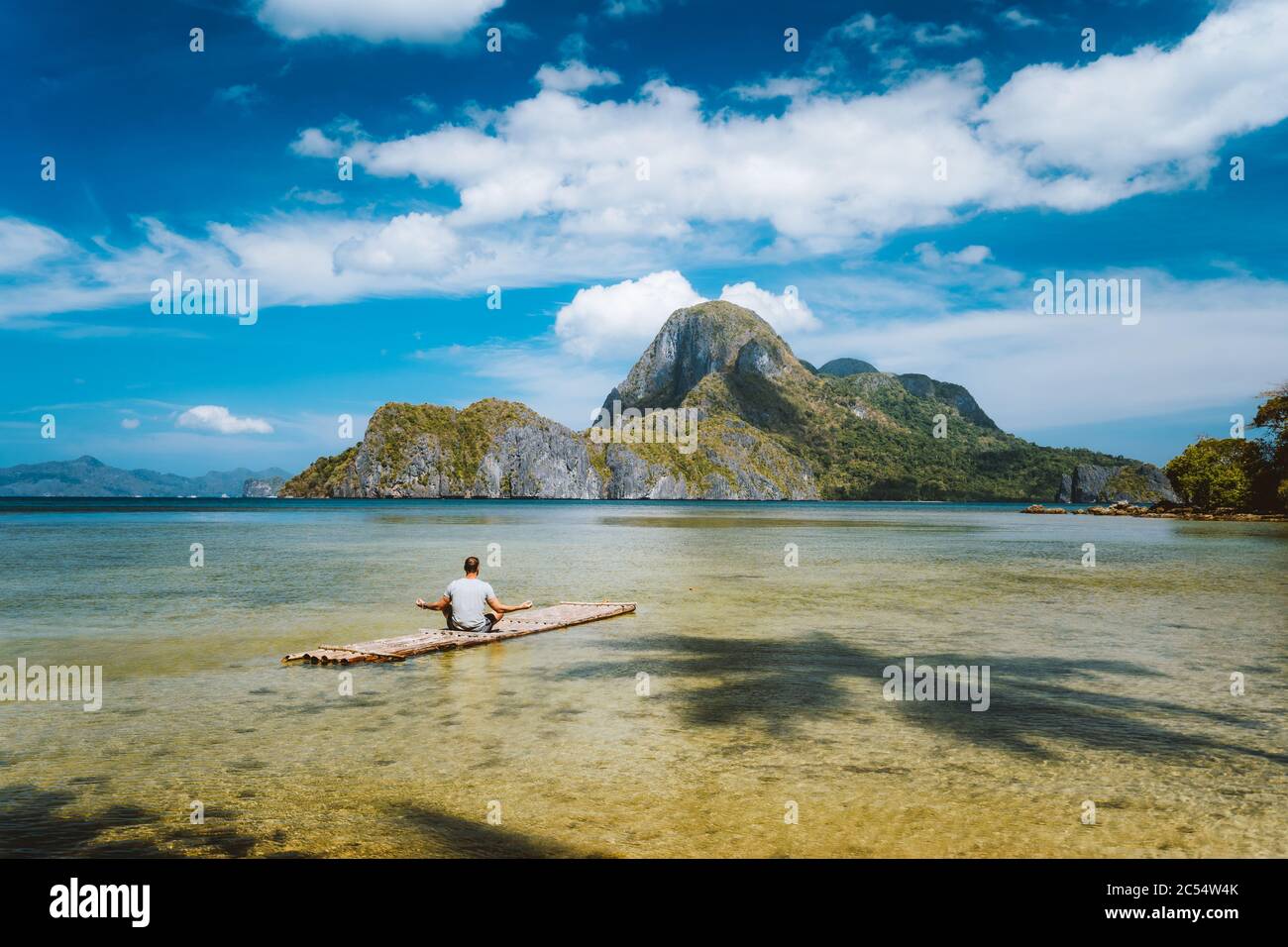 Der Mann, der auf Bambus meditiert, schwimmt umgeben von flachem Lagunenwasser und Inseln der Cadlao-Bucht in einer Entfernung. Palawan, Philippinen. Urlaubsurlaub Stockfoto