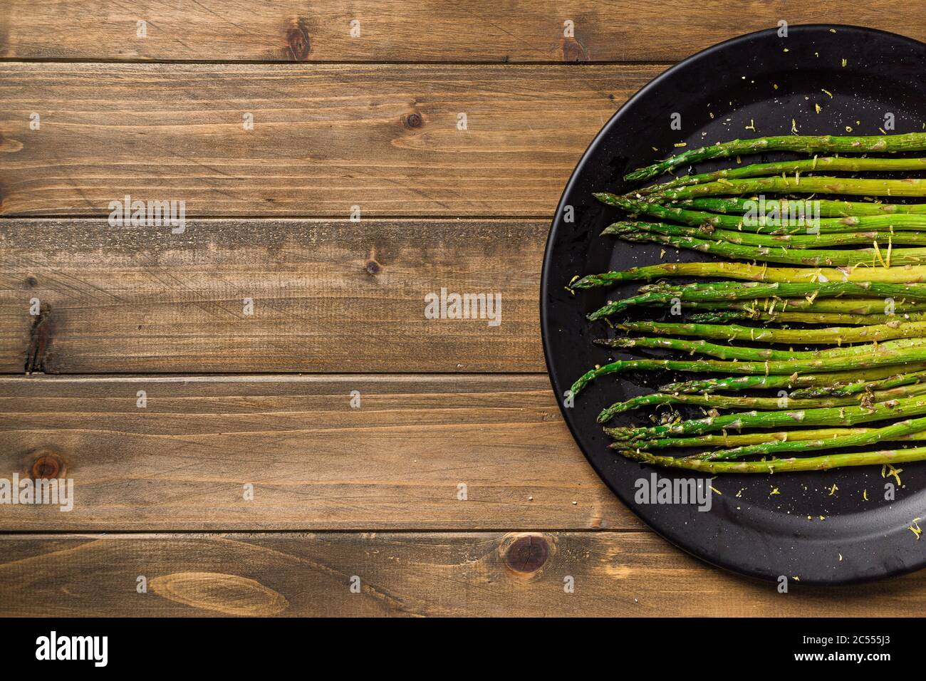 Spargel auf Holzhintergrund. Gesunde Ernährung ist mit diesem hausgemachten veganen Gericht einfach; gebratener Spargel mit Zitronenschale darauf. Das Gemüse ist s Stockfoto