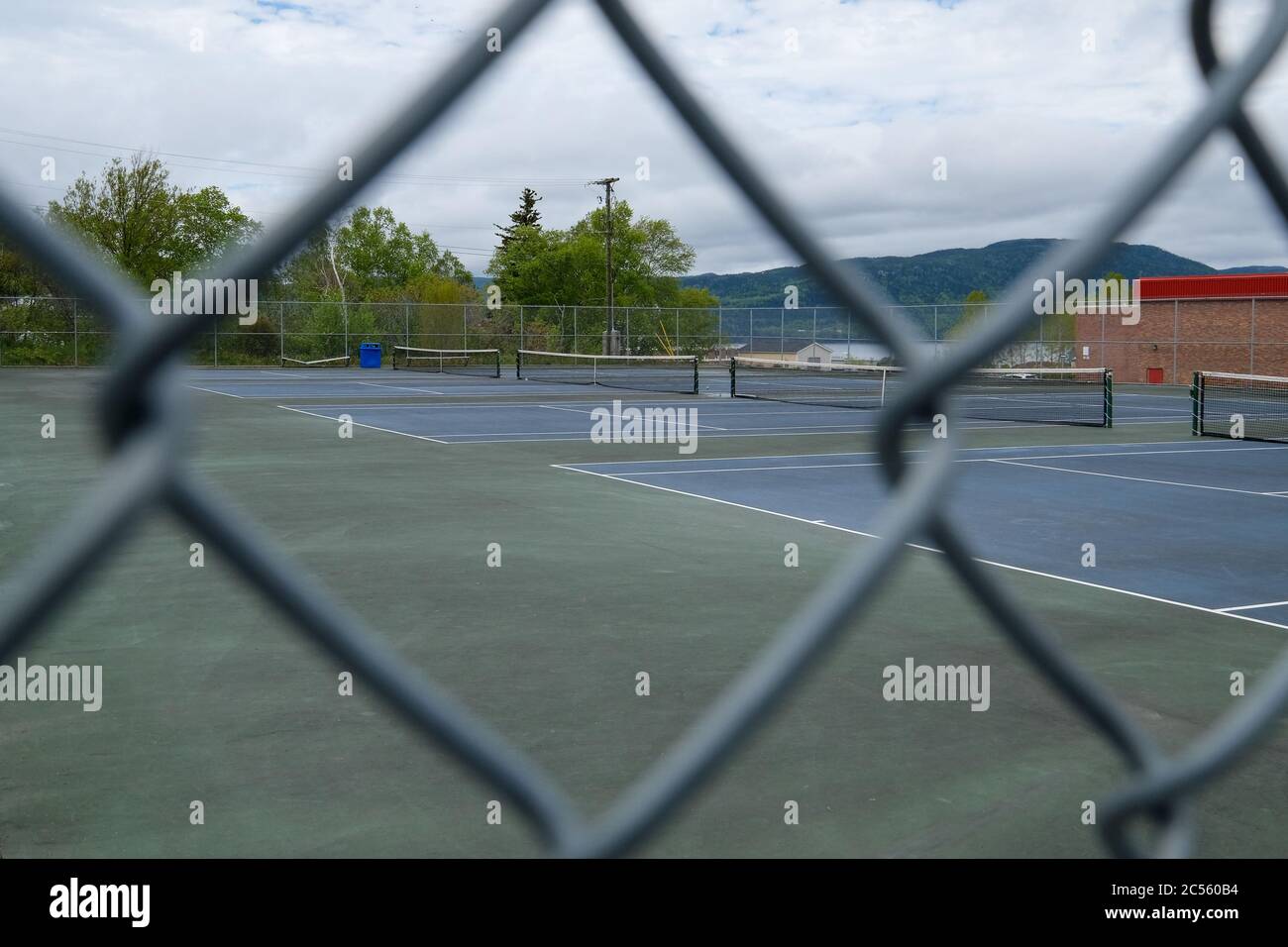 Mehrere Tennisplätze im Freien unter einem hellen, bewölkten Himmel. Die Gerichte sind blau gestrichen und sie haben jeweils ein Netz, das die Gerichte teilt. Stockfoto