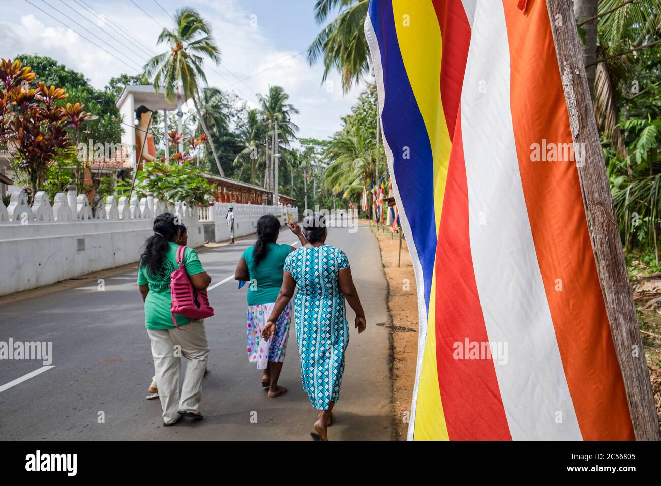 Kleine Gruppe von Frauen geht entlang einer offenen Straße vorbei an einem buddhistischen Tempel, Sri Lanka Stockfoto