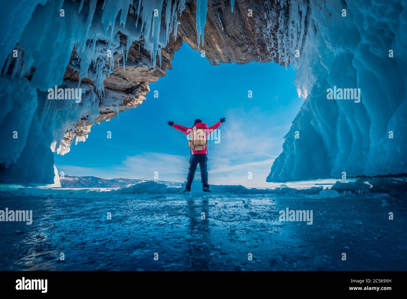 Reisender Mann tragen rote Kleidung und heben Arm auf gefrorenem Wasser in Eishöhle am Baikalsee, Sibirien, Russland stehen. Stockfoto