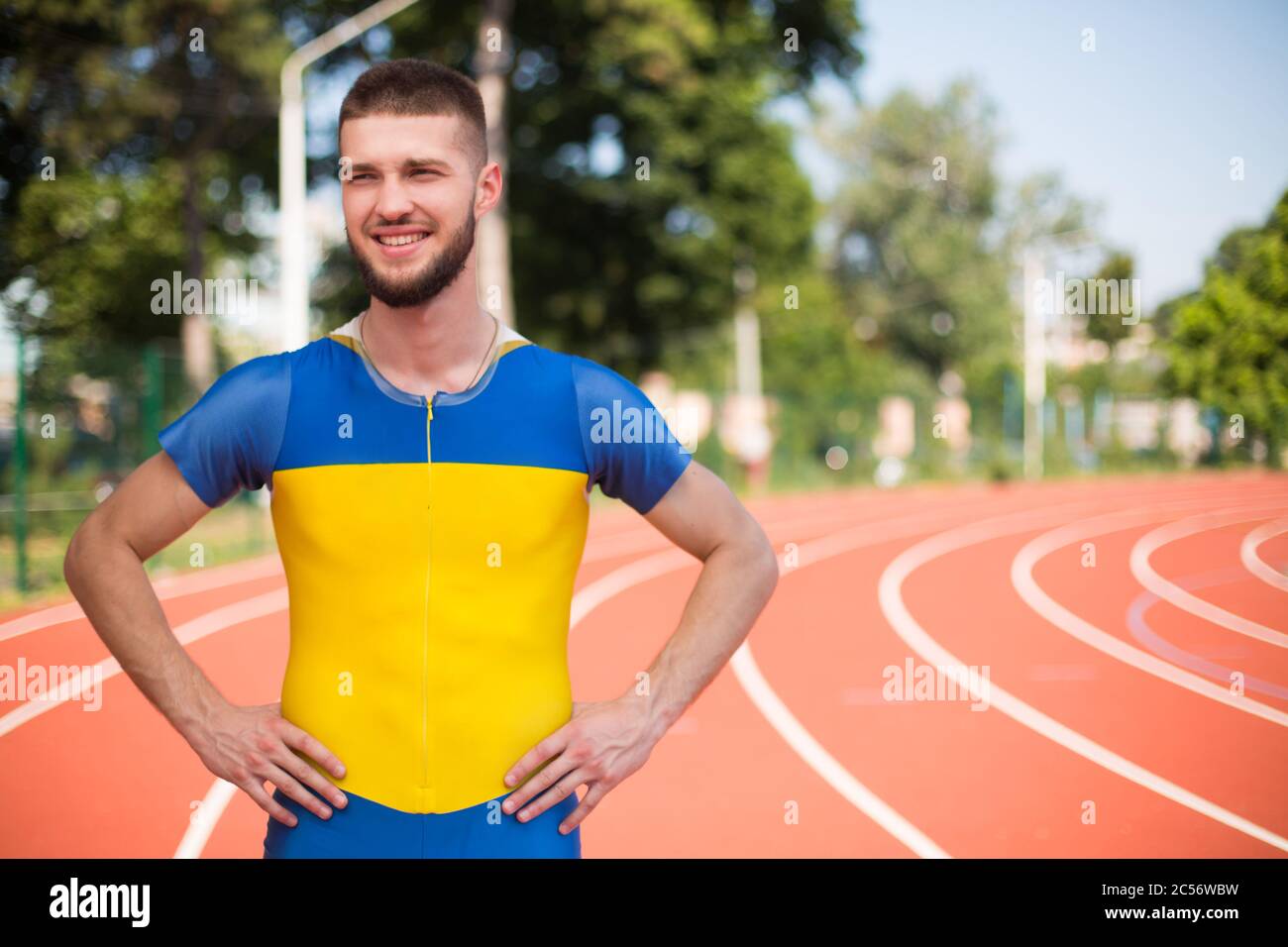 Der junge Profi-Sportler schaut glücklich beiseite, während er Zeit auf dem Laufband des Stadions verbringt Stockfoto