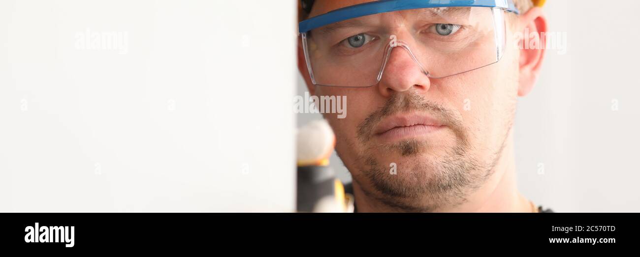 Reparaturmann in Helm und Maske, misst das Maßband Stockfoto