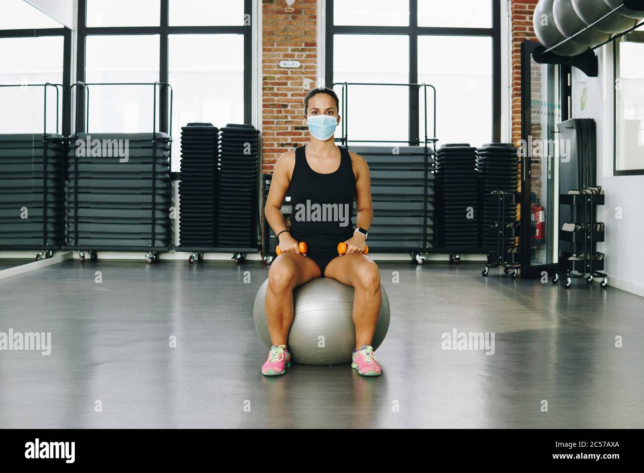 Junge dunkelhaarige Frau bereitet sich auf Pilates-Klasse im Fitnessstudio. Sie trägt eine Maske. Stockfoto