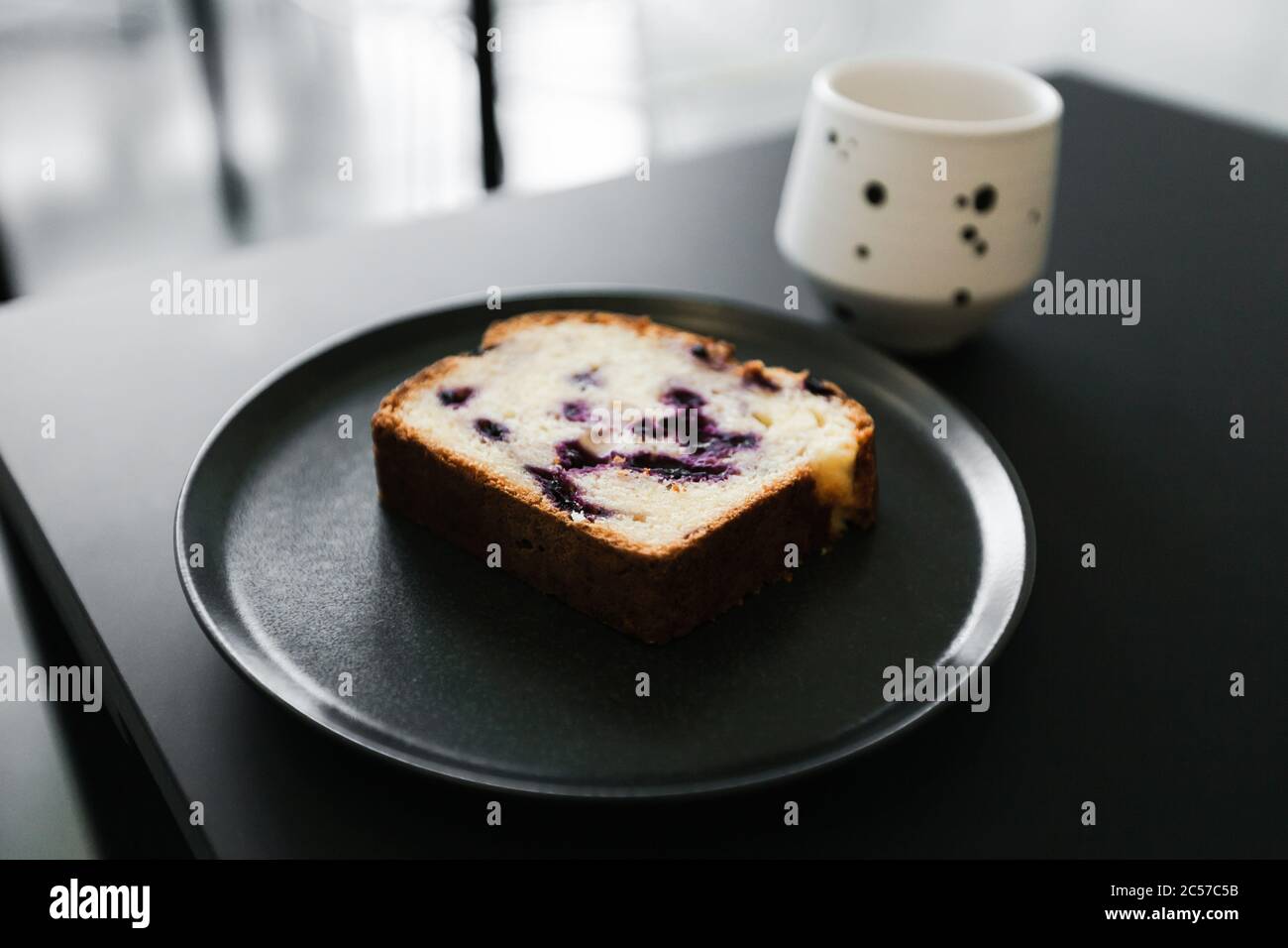 Ein Stück Obstkuchen mit Beeren und eine Tasse Kaffee auf einem schwarzen Tisch Stockfoto